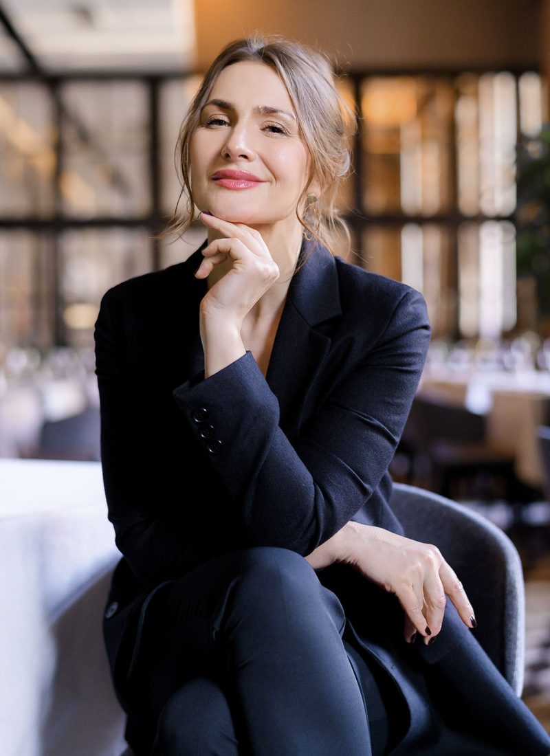 Portrait of smiling successful businesswoman looking into camera sitting in the restaurant. Business lady with stylish hairstyle wears elegant suit. Business meeting. Attractive appearance